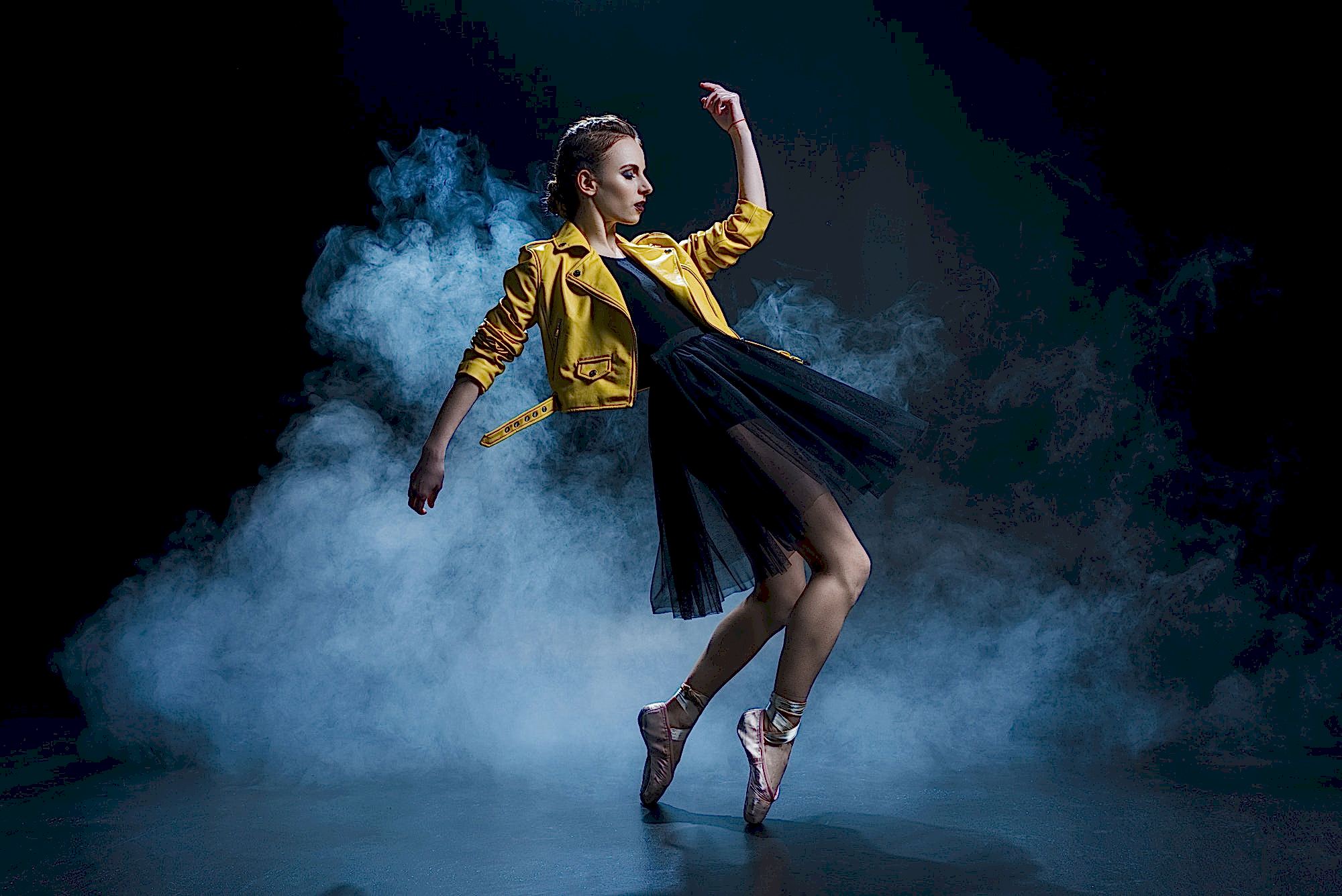 attractive girl dancing in pointe shoes and black tutu and yellow leather jacket in studio with